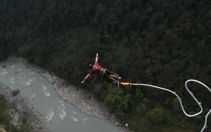 Bungee jumper in mid-fall above a river gorge