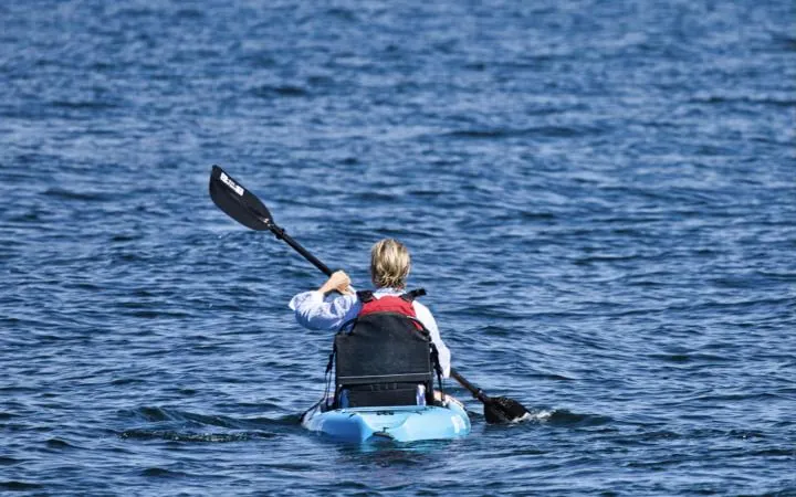 Kayaker in a life jacket paddling across blue water
