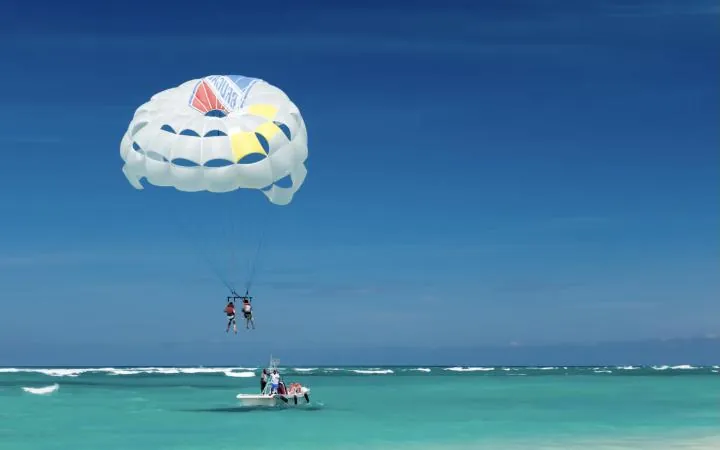 Two people parasailing above a turquoise sea behind a speed boat
